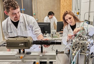 Three researchers wearing white lab coats, working with machinery and digital screens in the University of 鶹ý Advanced Engineering Centre